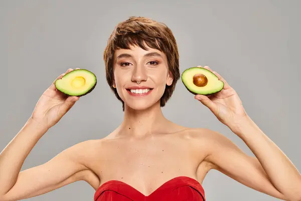 Uma mulher jovem graciosamente mantém duas metades de um abacate. — Fotografia de Stock