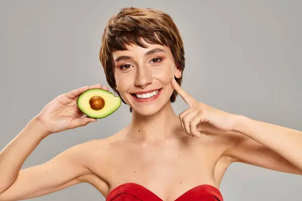 Жінка грайливо ховає обличчя за свіжим авокадо. — стокове фото