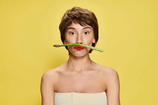 Elegant woman holds asparagus near mouth, against vibrant backdrop. — Stock Photo