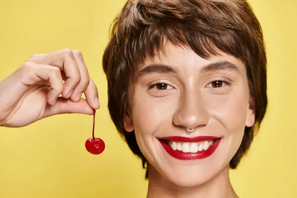 Woman holding a cherry close to her face on a colorful backdrop. — Stock Photo