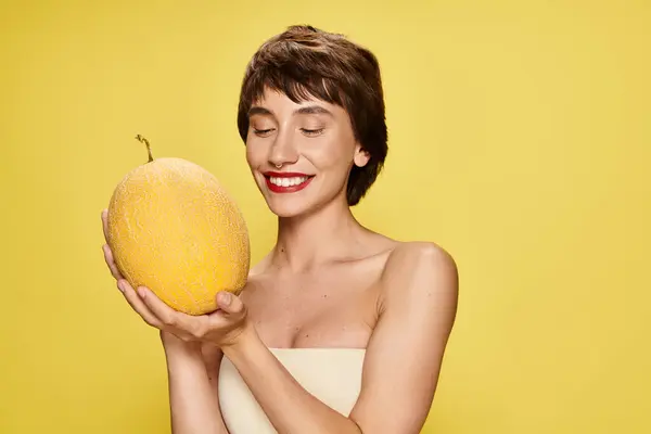 A captivating young woman in a white dress gracefully holds a ripe melon against a vibrant backdrop. — Stock Photo