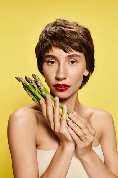 A woman playfully hides her face with a bunch of fresh asparagus. — Stock Photo