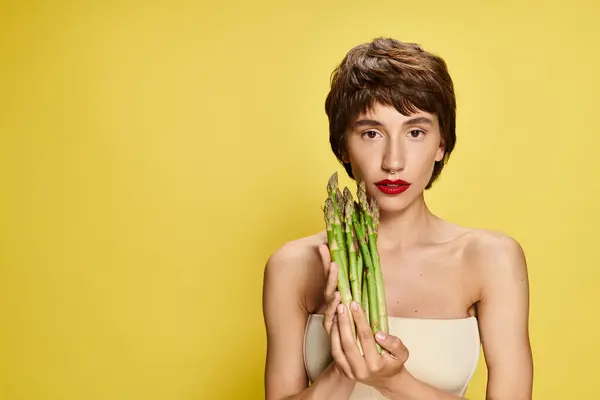 Una donna si nasconde giocosamente il viso dietro un fascio di asparagi freschi. — Foto stock