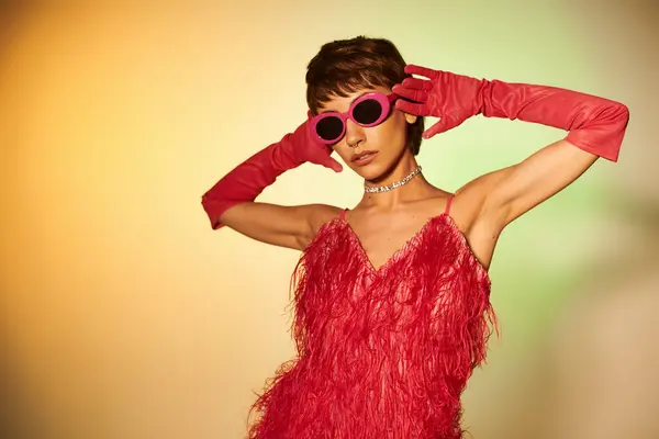 A fashionable young woman in a red dress and red gloves strikes a pose on a vibrant backdrop. — Stock Photo