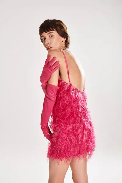 Una giovane donna alla moda posa in un elegante abito rosa e guanti su uno sfondo vibrante. — Foto stock