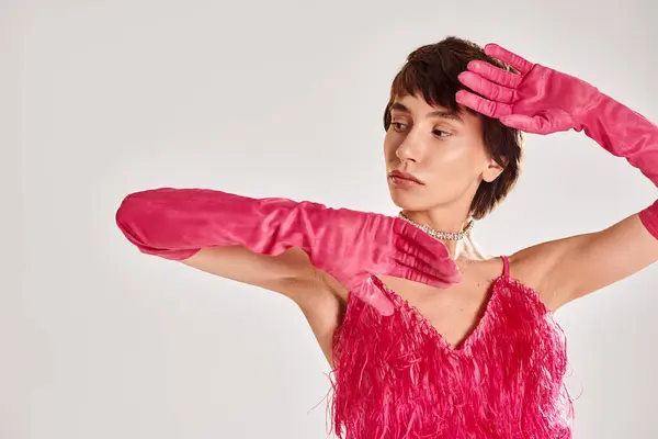Eine modische junge Frau in rosa Kleid und passenden Handschuhen posiert elegant vor einer lebendigen Kulisse. — Stockfoto