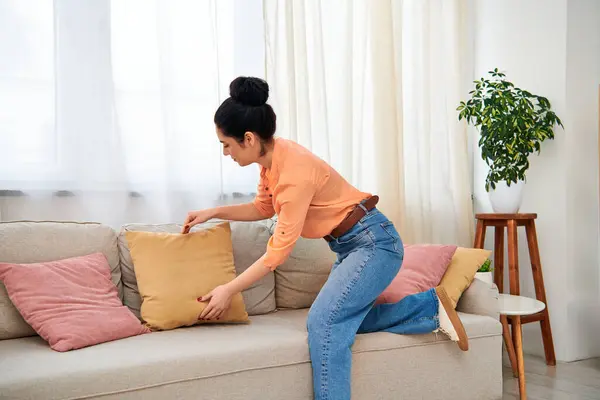 Una mujer con estilo en ropa casual se sienta con gracia en un sofá, agarrando una almohada acogedora. - foto de stock