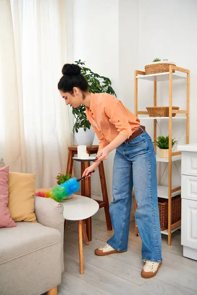 Una mujer elegante con atuendo casual limpia meticulosamente una sala de estar con una fregona, creando un ambiente sereno. - foto de stock
