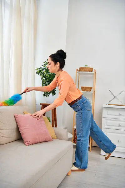 Une femme élégante en tenue décontractée nettoie diligemment un canapé avec une serpillière, éclaircissant son espace à la maison. — Photo de stock