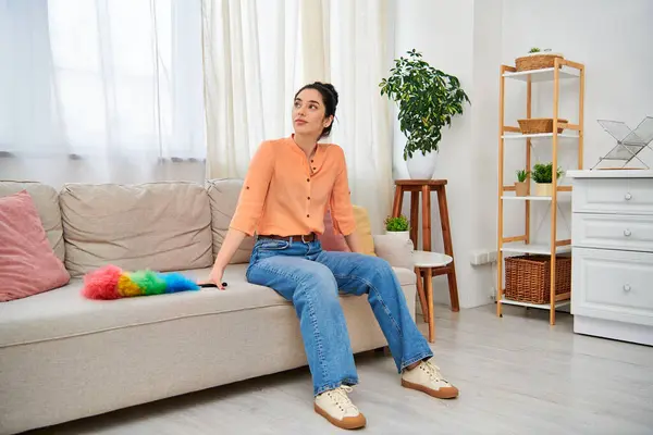 A stylish woman in casual attire relaxes on a plush couch in a modern living room. — Stock Photo