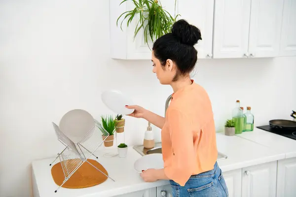 Una mujer elegante con atuendo casual de pie en un mostrador de cocina, sosteniendo un frisbee blanco. - foto de stock