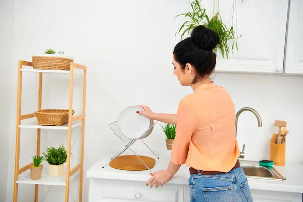 Une femme en tenue décontractée se tient à un évier de cuisine, engagée dans des tâches ménagères d'une manière sereine. — Photo de stock