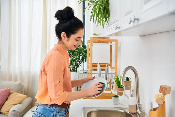 A stylish woman washes dishes in the cozy kitchen of her home, embodying grace in every movement. — Stock Photo