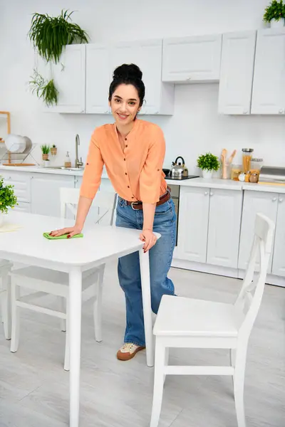 Una mujer con estilo, en atuendo casual, está junto a una mesa blanca y una silla, exudando una sensación de sofisticación y limpieza. - foto de stock