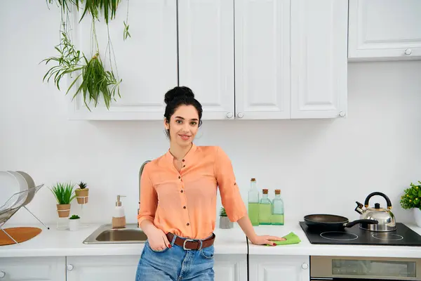 A stylish woman in casual attire standing in a kitchen next to a sink. — Stock Photo