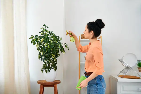 Una mujer con estilo en una camisa naranja limpia cuidadosamente una planta, mostrando amor y cuidado por su ambiente hogareño. - foto de stock