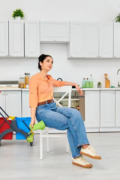 Una mujer elegante con atuendo casual sentada cómodamente en una silla en una acogedora cocina. - foto de stock