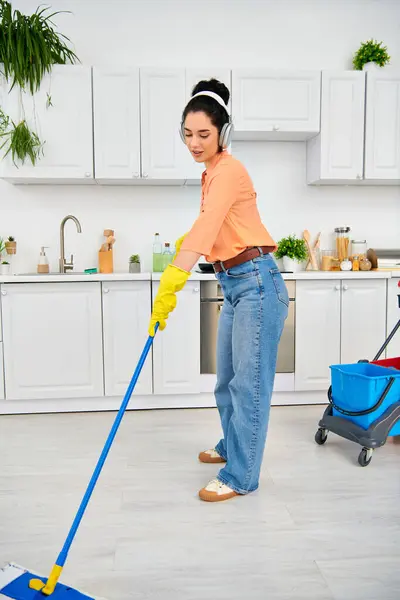 Una mujer elegante con ropa casual limpia elegantemente el piso de la cocina con una fregona, exudando elegancia y funcionalidad. - foto de stock