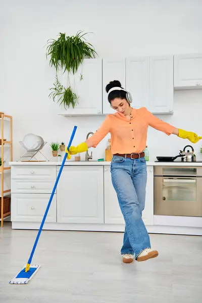 Una mujer elegante con atuendo casual limpia elegantemente el suelo con una fregona en su casa. - foto de stock