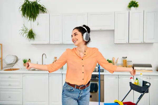 A stylish woman in headphones stands in a kitchen. — Stock Photo