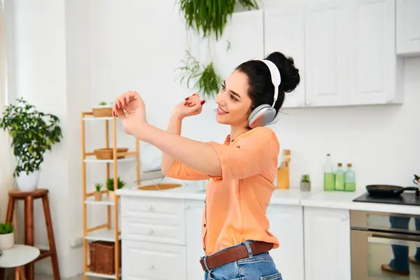 Uma mulher elegante usando fones de ouvido fica em uma cozinha acolhedora, multitarefa entre a limpeza e ouvir música. — Fotografia de Stock