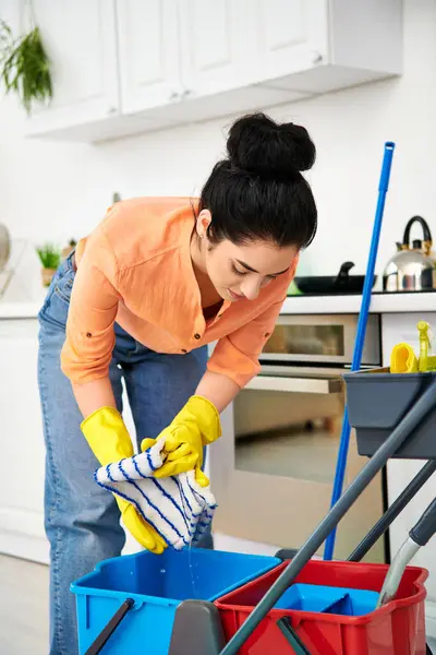 Стильна жінка в повсякденному одязі ретельно чистить підлогу мопедом і відром. — стокове фото