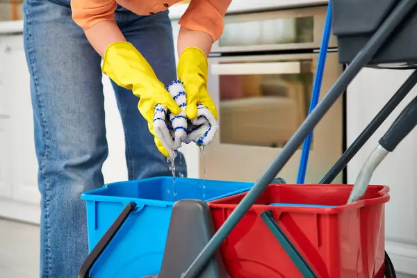 Una mujer elegante en ropa casual limpia elegantemente el piso con un cubo, asegurando un ambiente limpio y ordenado en el hogar. - foto de stock