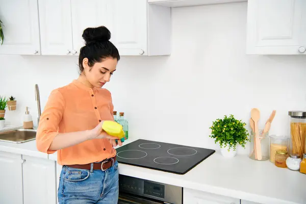 A stylish woman in casual attire standing in a kitchen, holding a bright yellow frisbee. — Stock Photo