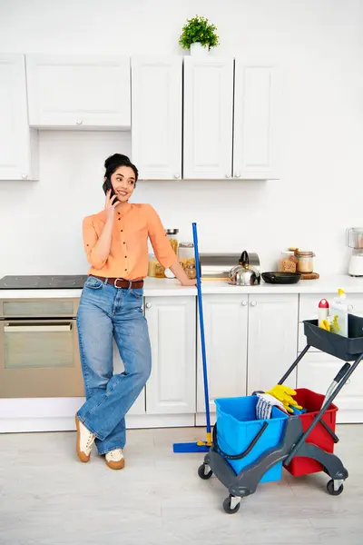 Eine stilvolle Frau in legerer Kleidung steht in einer Küche und telefoniert mit einem Handy. — Stockfoto