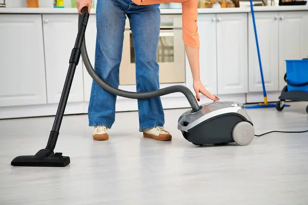 Eine stilvolle Frau in lässiger Kleidung saugt anmutig den Küchenboden. — Stockfoto