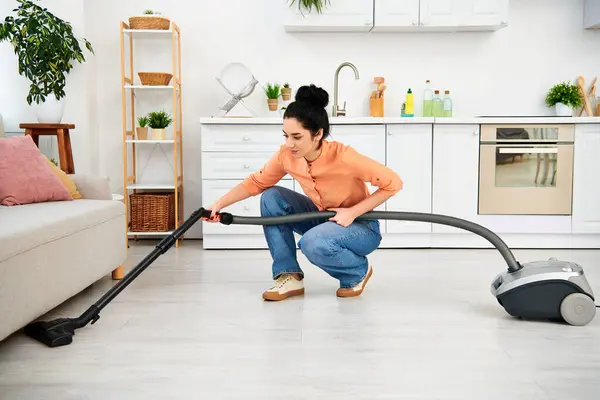 A stylish woman in casual attire gracefully vacuums the floor with her sleek vacuum cleaner, bringing cleanliness to her home. — Stock Photo