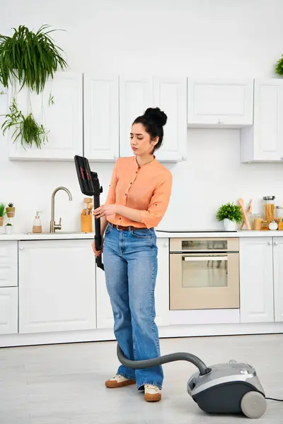 Una mujer elegante con atuendo casual aspira elegantemente el suelo de la cocina, aportando un toque de elegancia a las tareas cotidianas del hogar. — Stock Photo