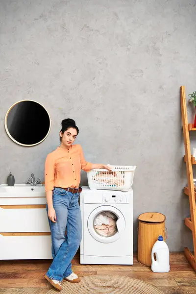 Uma mulher casualmente vestida ao lado de uma máquina de lavar roupa, cuidando de suas tarefas domésticas. — Fotografia de Stock