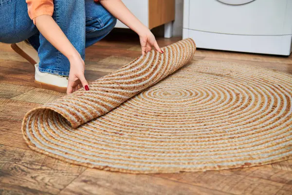 Eine Frau kniet neben einem Teppich, lässig gekleidet, und putzt ihr Haus in gelassener und zielgerichteter Weise.. — Stockfoto