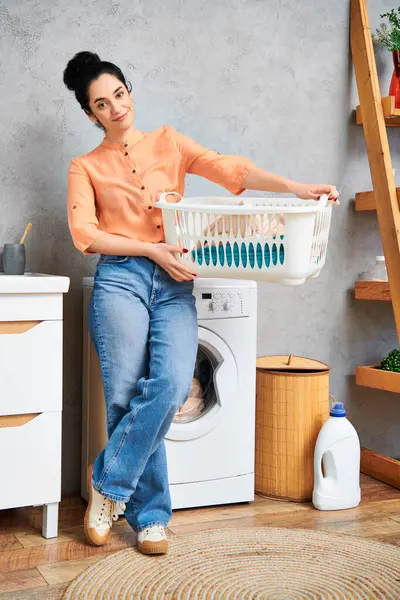 Eine stilvolle Frau in Freizeitkleidung hält einen Wäschekorb neben einer Waschmaschine. — Stockfoto
