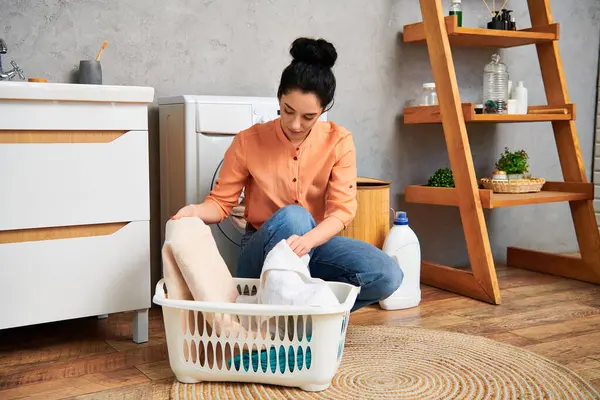 Eine stilvolle Frau sitzt mit einem Wäschekorb vor sich auf dem Fußboden und erledigt mit Anmut und Eleganz Haushaltsarbeiten. — Stockfoto