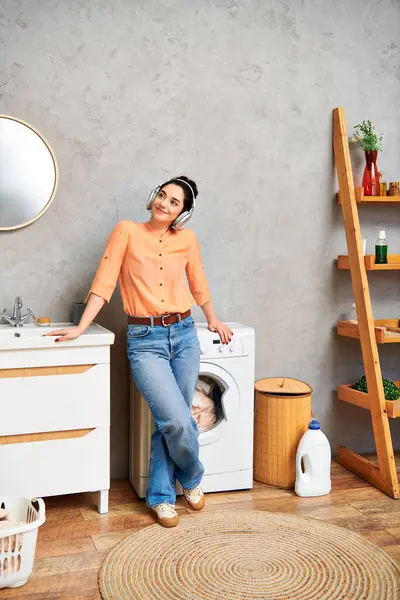 Стильна жінка в повсякденному вбранні витончено стоїть поруч з пральною машиною в домашній ванній. — стокове фото
