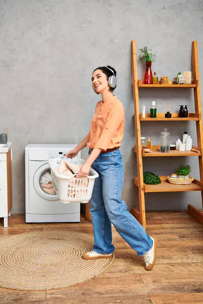 Una donna elegante in abbigliamento casual tiene felicemente un cesto di lavanderia, irradiando positività ed energia. — Foto stock