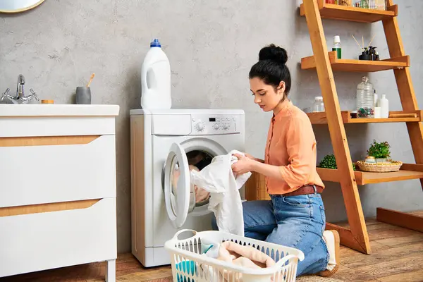Una mujer elegante con atuendo casual sentada al lado de una lavadora, tomando un momento de calma en medio de la tarea de lavar la ropa. - foto de stock