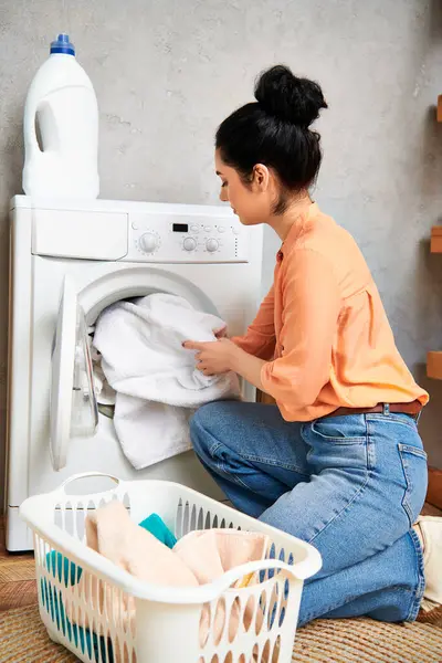 Una donna elegante in abbigliamento casual si siede accanto a una lavatrice, focalizzata sulla pulizia della sua casa. — Foto stock
