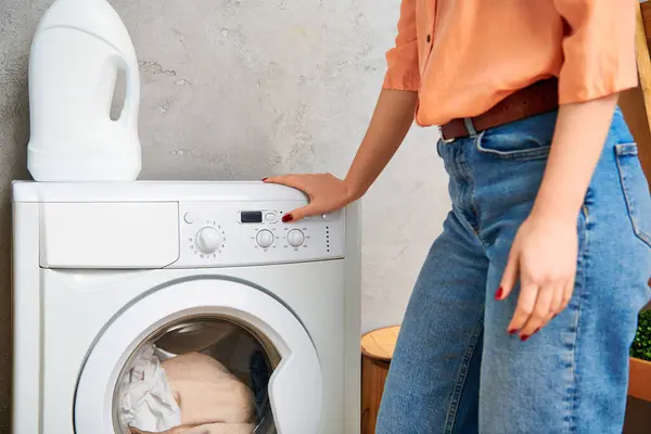 Une femme élégante en tenue décontractée se tient avec confiance à côté d'une machine à laver moderne, prête à s'attaquer à sa corvée de blanchisserie. — Photo de stock