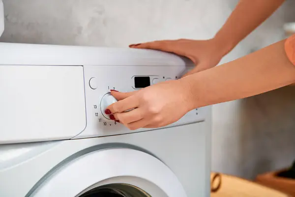 Una mujer elegante con atuendo casual sujeta cuidadosamente un botón a una lavadora. - foto de stock