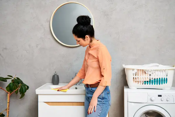 Una mujer con estilo y atuendo casual de pie frente a una lavadora, lista para hacer frente a las tareas domésticas. - foto de stock