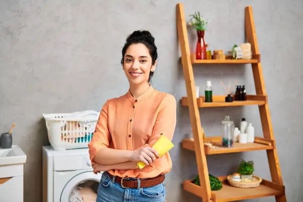 Una mujer con estilo y atuendo casual se para junto a una lavadora en un baño, enfocada en hacer la colada. - foto de stock