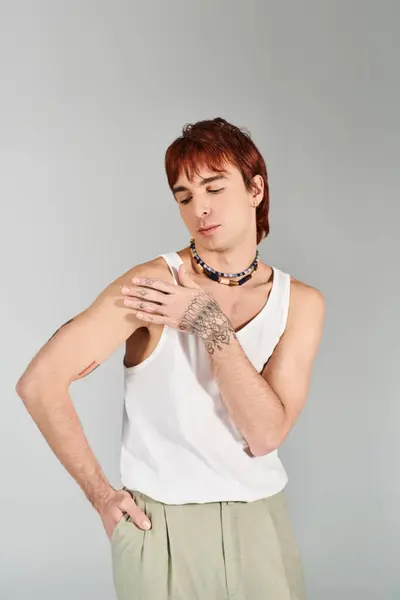 A stylish young man poses confidently in a white tank top and khaki shorts against a grey studio background. — Stock Photo