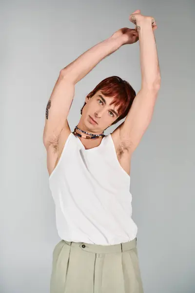 A fashionable young man strikes a pose in a studio, dressed in a white tank top and khaki pants against a grey background. — Stock Photo