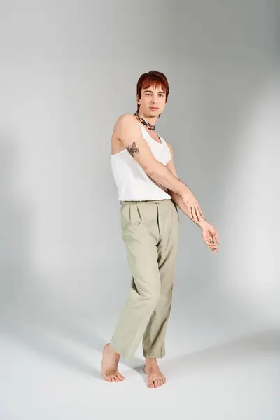 Ein stilvoller junger Mann posiert in einem Studio vor grauem Hintergrund, trägt ein weißes Tank-Top und eine khakifarbene Hose. — Stockfoto