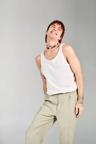 A stylish young man poses confidently in a studio setting, wearing a white tank top and khaki pants against a grey background. — Stock Photo