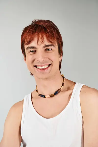 A stylish young man with red hair striking a pose in a white tank top against a grey studio backdrop. — Stock Photo
