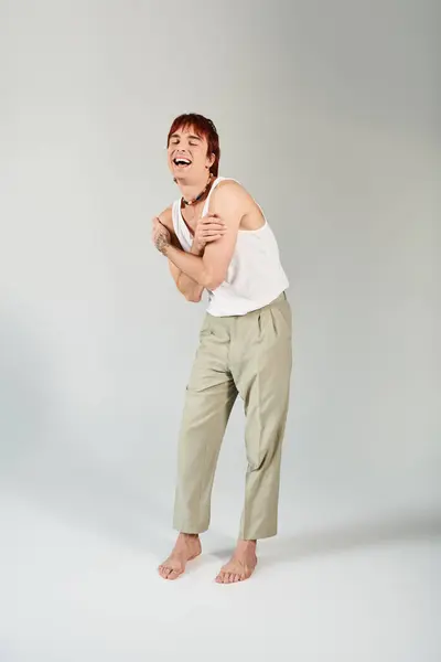 A stylish young man in a white tank top and khaki pants strikes a pose in a studio setting with a grey background. — Stock Photo